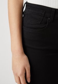 Blugi din denim negri cu un design ajustat, având o buzunar frontal și detalii de cusătură vizibile lângă talie și buzunarul din spate.
