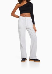 Vita cargo byxor med flera fickor, kombinerat med en svart topp med en axel. Kläderna har en figurnära design och en lös passform överlag.