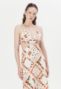 Bloemendruk jurk met een cropped top met spaghettibandjes en uitsparing aan de zijkanten, gemaakt van lichtgewicht stof in crème met oranje accenten.