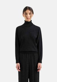 Maglione a collo alto nero in texture a coste, maniche lunghe, aderente in vita, abbinato a pantaloni neri coordinati. Design semplice e minimalista.