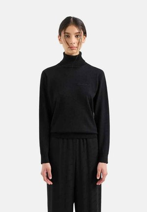 Maglione a collo alto nero in texture a coste, maniche lunghe, aderente in vita, abbinato a pantaloni neri coordinati. Design semplice e minimalista.
