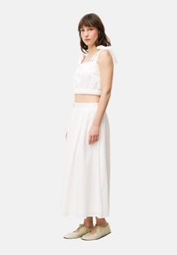 Witte cropped top met strikbandjes, elastische tailleband, gecombineerd met een lange witte rok met een gestructureerd patroon. Model draagt beige schoenen.