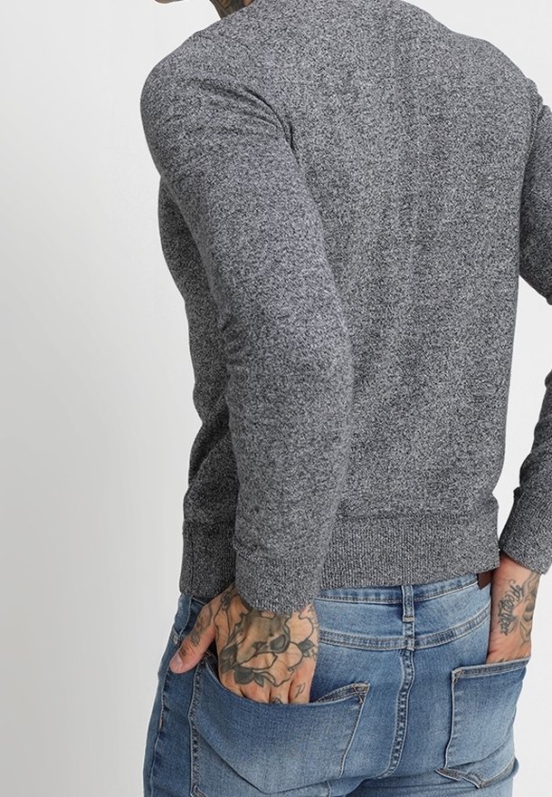 Grå, texturerad tröja med långa ärmar och en figurnära nederkant, bärs med blå denimjeans som har bakfickor.