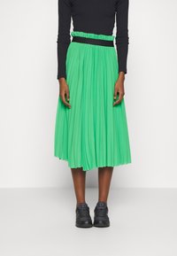 Jupe midi plissée verte avec une taille élastique, assortie à des baskets sombres. Le tissu semble léger et fluide.