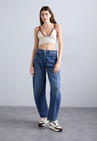 Heklet bralette i krem med bordeaux-kant, sammen med blå løse jeans og flerfargede sneakers med teksturert såle.