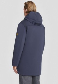 Navyblauwe, capuchonjack van zachte stof; heeft een relaxte fit, lange mouwen en een subtiel logo op de mouw; gladde textuur.