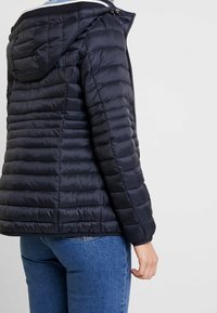 Doudoune marine à design matelassé horizontal, capuche ajustée et fermeture éclair. Texture lisse avec une apparence légère et isolée.