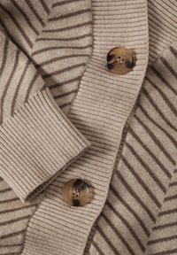Beige svetr s hnědými vertikálními pruhy, ribbed texturou na manžetách a velkým kulatým detailem z želvoviny na knoflíku.