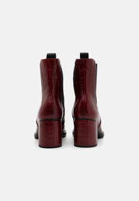 Botine din piele sintetică burgundă cu aspect de crocodil, cu toc pătrat, elastice laterale și un design elegant. Suprafață texturată cu accente negre contrastante.