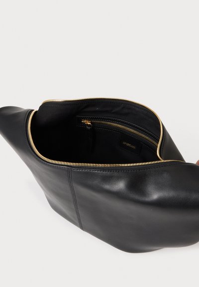 Pochette en cuir noir avec fermeture éclair dorée partiellement ouverte, montrant un compartiment zippé plus petit à l'intérieur avec une doublure en tissu de marque.