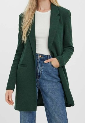 Blazer vert en tissu doux, avec un col cranté, une poche avant unique et une ouverture à l'avant, assorti à un jean bleu taille haute.