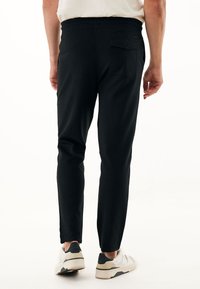 Černé tapered joggers s elastickým pasem, se zadní kapsou a hladkou texturou látky, doplněné bílými teniskami.