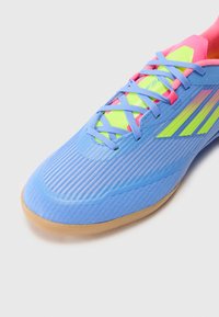 Világoskék sportcipő textúrált felülettel, rózsaszín és neon zöld részletekkel, valamint gumitalppal. Fűzős kivitel jellemzi.