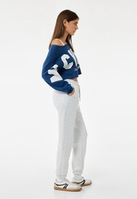 Blå kortärmad sweatshirt med vit text, matchad med ljusgrå byxor och vita sneakers med svarta accenter. Mjuk tygkänsla och passform.
