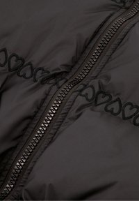 Zwarte gewatteerde jas met een centrale ritssluiting en borduursels van harten langs de ritssluiting, gemaakt van een gladde tekstuurstof.