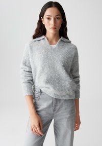 Lichtgrijze wollen blendtrui met een v-hals en kraag, met een zachte, gebreide stof en geribbelde mouwen, gecombineerd met lichtgrijze jeans.