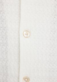 Tessuto bianco strutturato con un motivo intrecciato, con un bottone rotondo di colore chiaro visibile al centro.