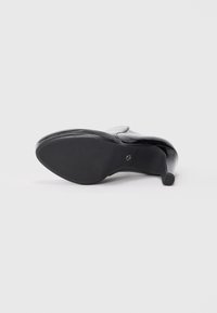Chaussure à talon haute noire avec un extérieur en cuir verni brillant. Dotée d'un bout pointu et d'un talon effilé. Semelle lisse et plate avec un minimum de détails.