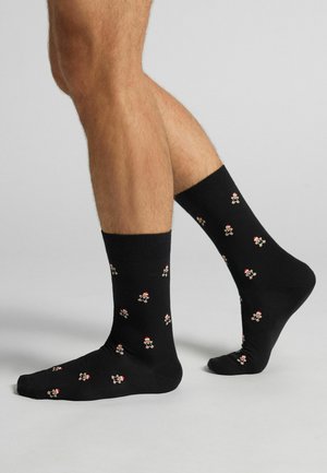 Calzini neri con un motivo ripetuto di piccoli omini di pan di zenzero con cappelli rossi e bianchi, realizzati in un materiale liscio ed elastico.