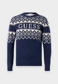 Maglione a maglia blu navy con un motivo geometrico in bianco e beige, con il nome del marchio "GUESS" ben in evidenza al centro.