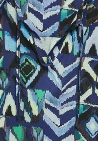 Färggs mönstrad tyg med geometriskt mönster i blå, grön och svart ton. Har en V-ringning och dragsko detaljer.