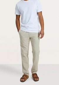 Lichtbeige Broek met een Relaxte Pasvorm, Gecombineerd met een Effen Witte T-shirt. De Outfit Inclusief Bruine Sandalen met Verstelbare Bandjes.
