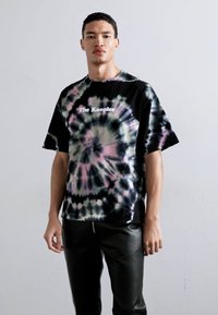 Svart tie-dye t-skjorte med spiral mønster i grønt og rosa, med merkevarenavnet "The Kooples" trykt i hvitt over brystet.
