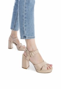 Sandalias de plataforma beige con un tacón grueso, correas cruzadas, correa ajustable al tobillo y una textura suave de gamuza.