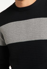 Schwarz-grauer gestreifter Strickpullover aus texturiertem Stoff; mit einem gerippten Rundhalsausschnitt und horizontalen Streifen in variierenden Breiten.