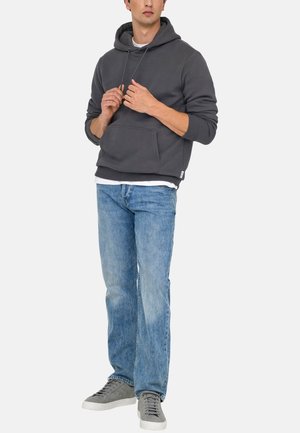Grijze katoenen hoodie met een kangoeroezak, trekkoordcapuchon en ribbelmanchetten, gedragen over een wit shirt, gecombineerd met lichtblauwe jeans en grijze sneakers.