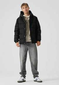 Sort pufferjakke med hætte, der har et quiltet design. Sammen med en beige sweatshirt, grå jeans og hvide sneakers med sorte striber.