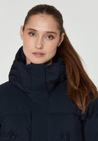 Chaqueta acolchada azul marino con cuello alto, que presenta un texturizado acolchado y cierre frontal. Tejido suave con un acabado liso.