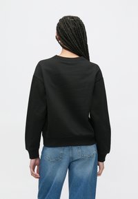 Czarna bluza o luźnym kroju, z prążkowanym dekoltem i ściągaczami na rękawach. Połączona z niebieskimi dżinsami o prostych nogawkach i tylnych kieszeniach.