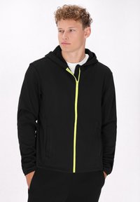 Zwarte zip-up hoodie met een neon groene rits, voorzien van een capuchon, dubbele zijzakken en een zachte textuur. Ontworpen voor casual draagstijl.
