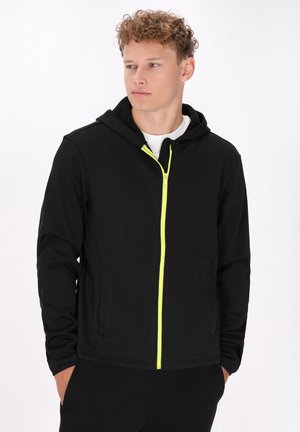 Zwarte zip-up hoodie met een neon groene rits, voorzien van een capuchon, dubbele zijzakken en een zachte textuur. Ontworpen voor casual draagstijl.
