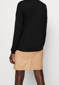 Czarny, luźny sweter o przedłużonym kroju z prążkowanym wykończeniem na dole i mankietach, zestawiony z dopasowaną, jasnobeżową skórzaną spódnicą z przeszyciem z przodu.