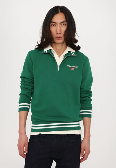 Grønn hettegenser med en fjerdedel glidelås, hvit polo-krage under, og hvite striper på ermene og kanten. Har "POLO SPORT" logo med et flagg.