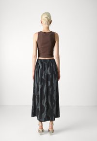 Top corto marrone abbinato a una lunga gonna nera con un motivo astratto grigio; sandali trasparenti con tacco completano l'outfit.