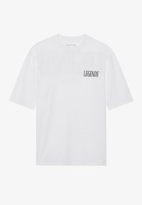 T-shirt blanc, à manches courtes, col rond, affichant le mot "LEGENDS" en police serif noire sur le côté supérieur gauche. Matériau en coton doux.