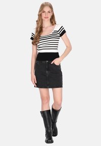 Zwart-wit gestreepte gebreide top met korte mouwen, gecombineerd met een zwarte denim minirok. Zwarte kniehoge laarzen maken de outfit compleet.