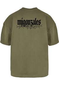 Oliven grøn oversized t-shirt med sort tekst "migonzales" og blomster- samt pigtrådsdesign på ryggen. Lavet af bomuldsstof, korte ærmer.