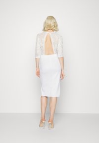 Vestido branco de renda com mangas de três quartos, design de costas abertas e silhueta midi ajustada. Corpete de renda texturizada com um acabamento liso na saia.