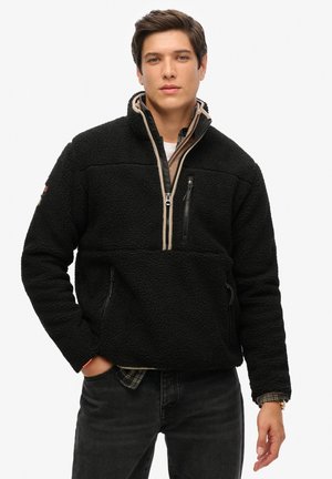 Zwart fleece pull met een halve ritssluiting, twee zijzakken en een borstzak. Kenmerkt zich door een gestructureerd oppervlak en lichte beige accenten.