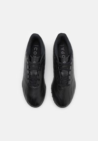 Chaussures de football noires en cuir, avec une surface texturée, un design incurvé, un bout rond, des lacets assortis et un détail de marque sur la semelle intérieure.