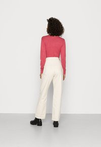 Camisa vermelha de mangas compridas combinada com calças largas de cintura alta em tom off-white. Botas pretas até ao tornozelo completam o visual.