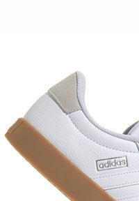Sneaker in pelle bianca con accenti in suede grigio, suola in gomma naturale e dettagli cuciti sui lati. Presenta il logo "adidas" di lato.