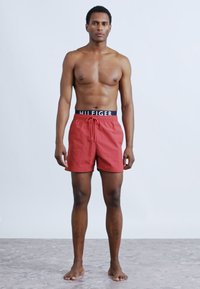 Κόκκινα μαγιό με κορδόνι και μαύρη ελαστική μέση με το λευκό κείμενο "HILFIGER". Το ύφασμα φαίνεται λείο και ελαφρύ.