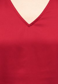 Κόκκινο ένδυμα με V-λαιμόκοψη που αφήνει να φαίνεται ένα μικρό τμήμα δέρματος στο πάνω μέρος του στήθους.