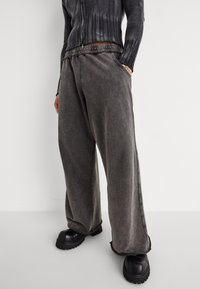 Weite graue Hosen mit strukturierter Oberfläche, ausgestattet mit einem gesteppten Bund und seitlichen Taschen. Kombiniert mit klobigen schwarzen Schuhen.
