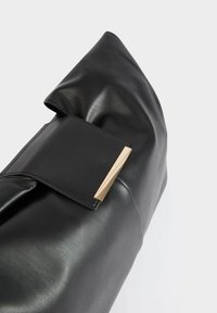 Borsa in pelle nera con un design piegato e una sezione superiore piatta con un accento in tono oro. Texture liscia senza motivi visibili.